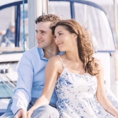 Couple sitting on a boat charter in NYC, smiling and holding hands with blue sky background.