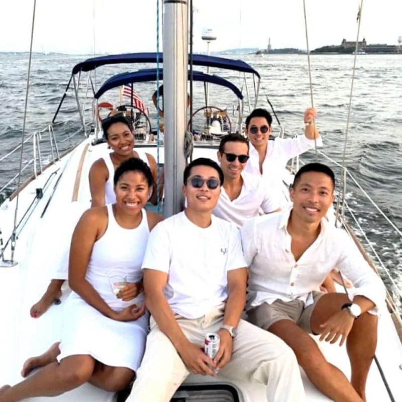 Group of six adults sitting on a sailboat, smiling during a corporate boat charter in NYC.