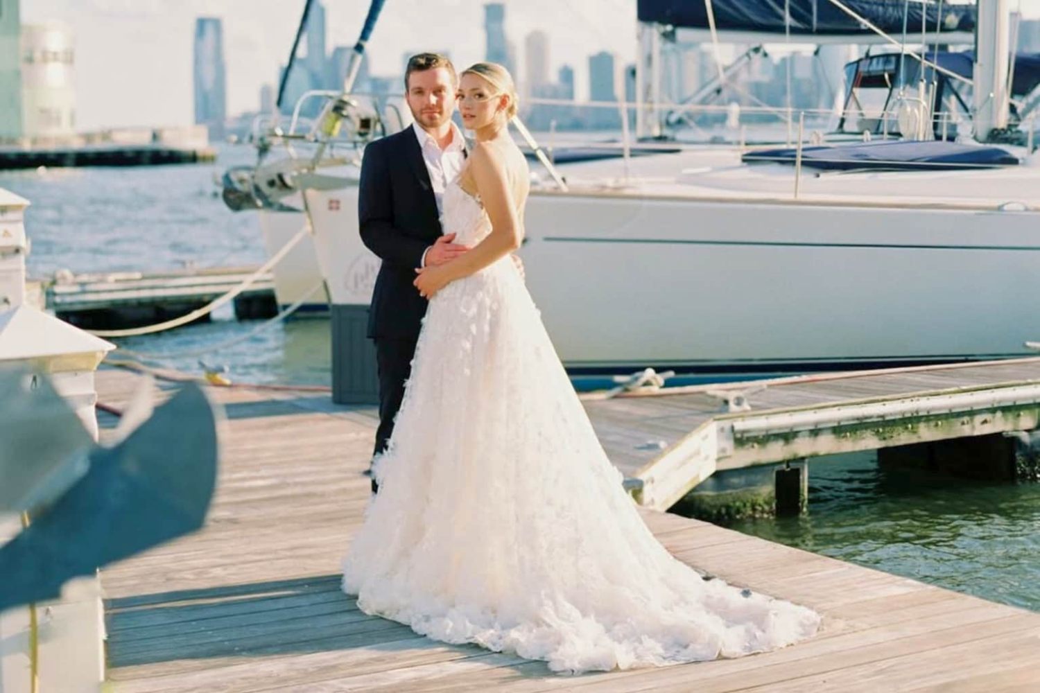 Bride and groom on a dock with rental boats and NYC skyline in the background.