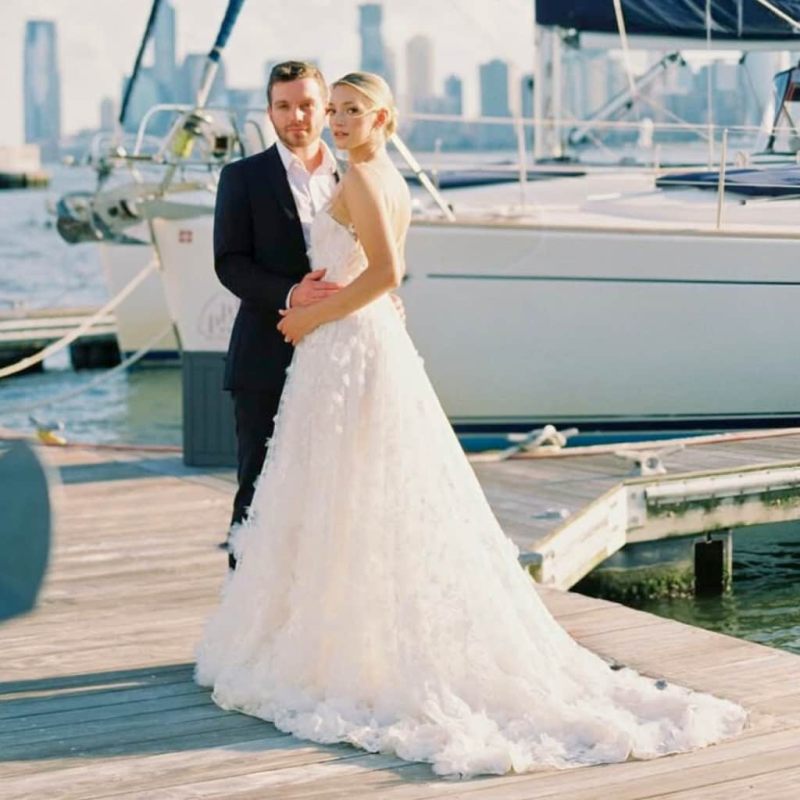 Bride and groom on a dock with rental boats and NYC skyline in the background.