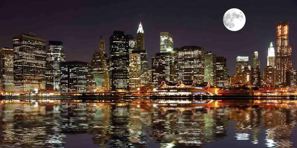 NYC skyline at night with bright full moon and reflections in water during sail.