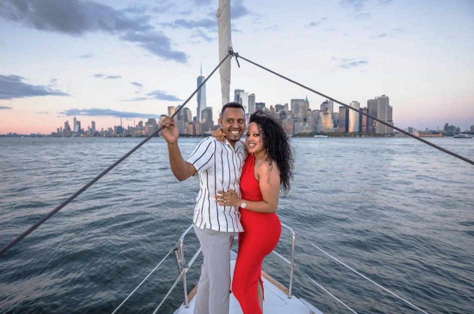 Couple smiling on the deck of a Manhattan boat charter with the city skyline in the background at sunset.