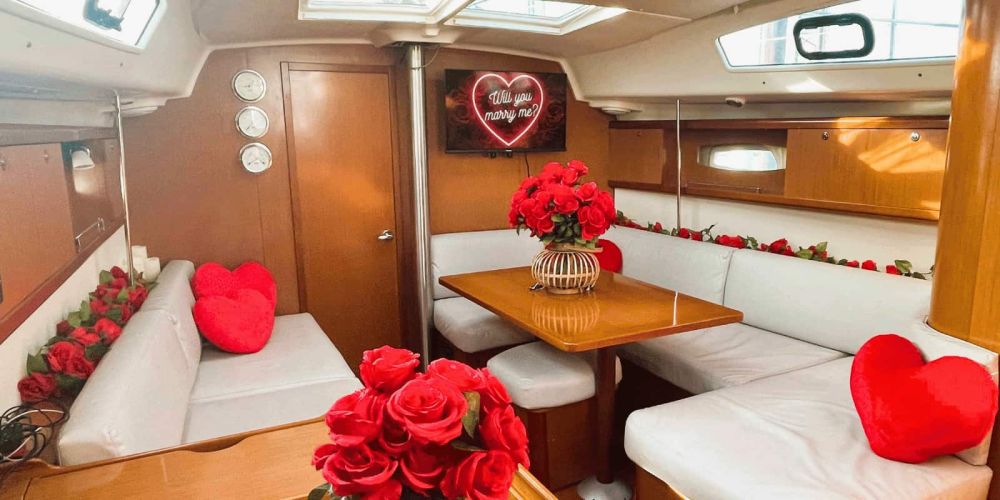 Boat cabin decorated with red roses and heart-shaped pillows, sign reads 'Will you marry me?'
