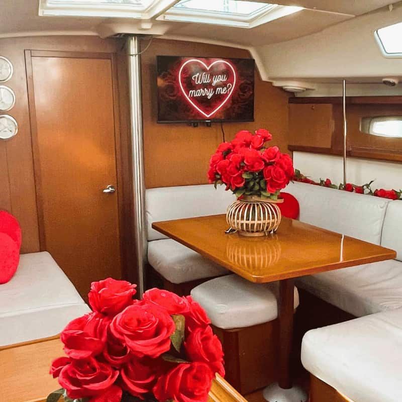 Boat cabin decorated with red roses and heart-shaped pillows, sign reads 'Will you marry me?'