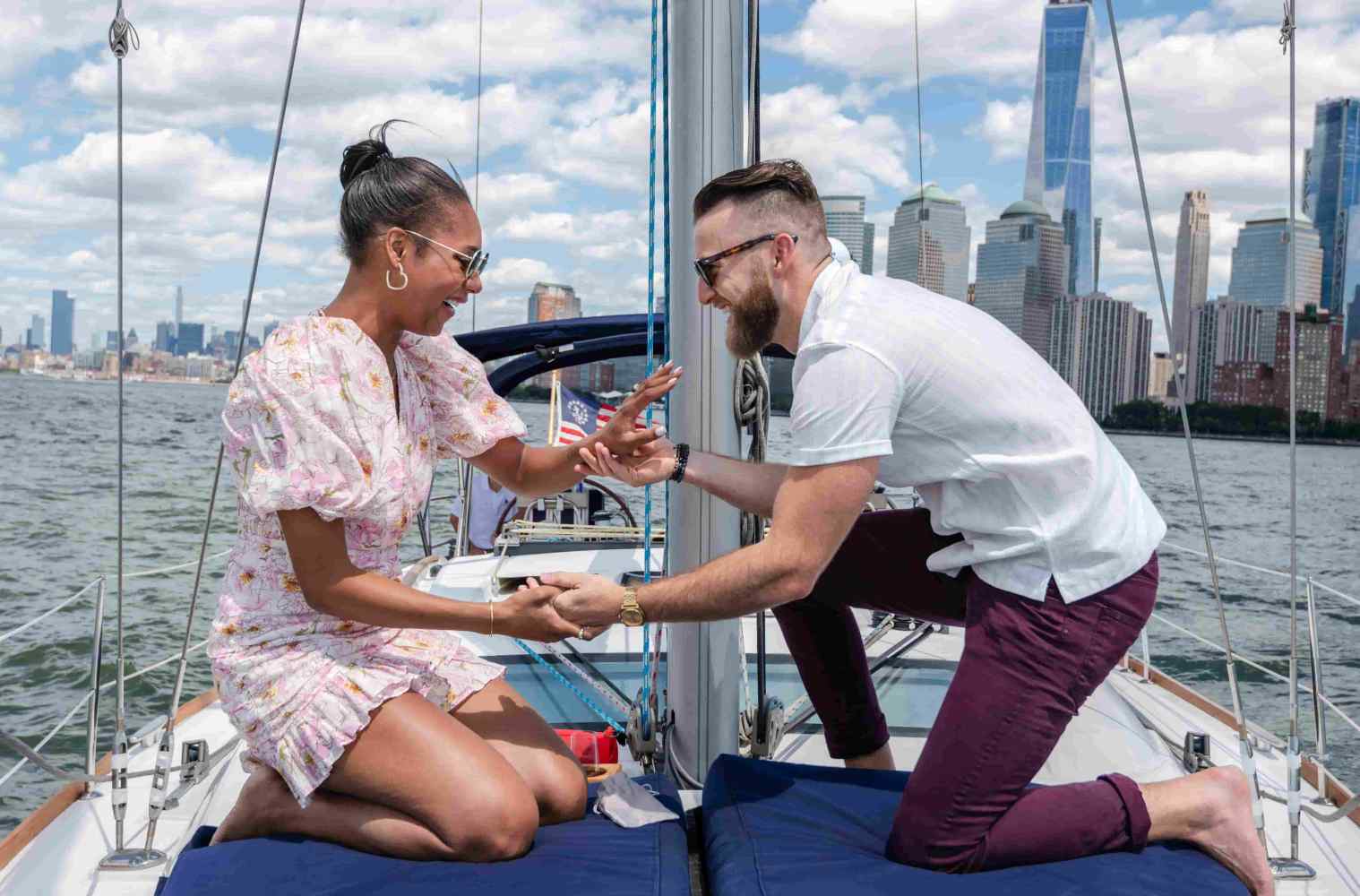 Man proposing to woman on a boat with the NYC skyline and water in the background.