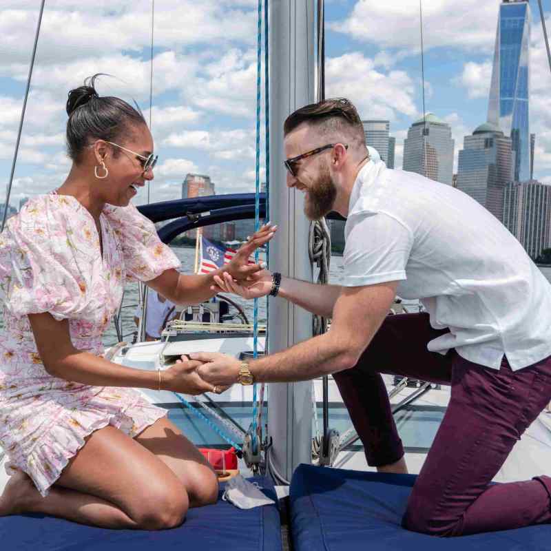 Man proposing to woman on a boat with the NYC skyline and water in the background.
