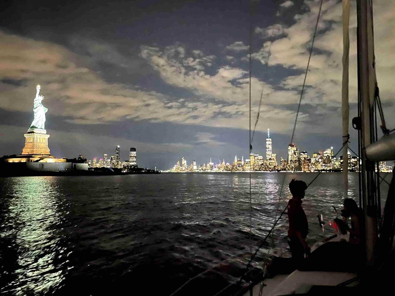 Sailboat at night with Statue of Liberty and NYC skyline in background during a night cruise in NYC.