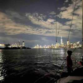 Sailboat at night with Statue of Liberty and NYC skyline in background during a night cruise in NYC.