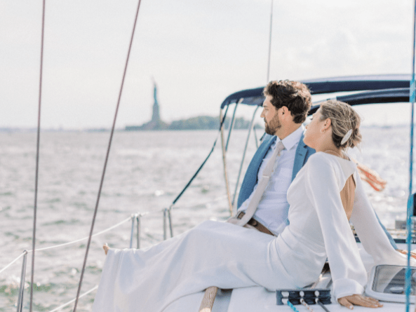 Couple in formal attire sits on a sailboat charter near the Statue of Liberty in NYC.