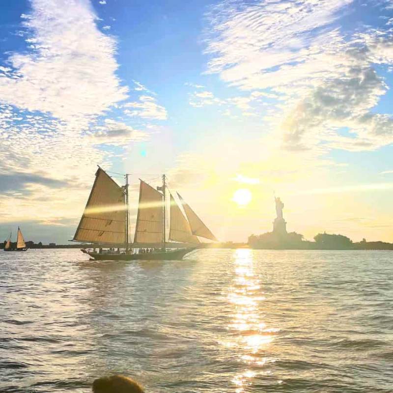 Private sunset sail in NYC at sunset with Statue of Liberty in the background and scattered clouds in sky.