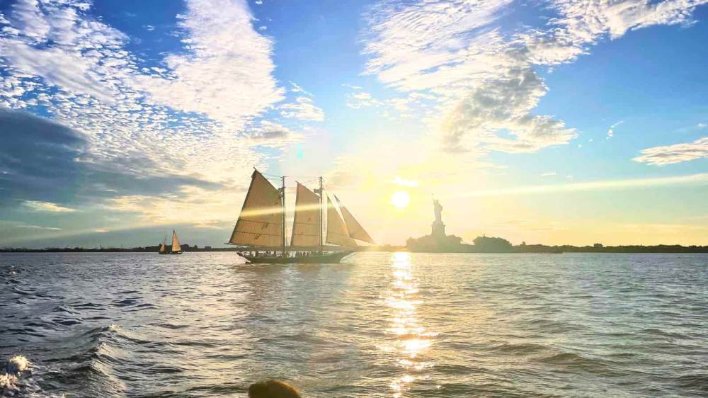 Private sunset sail in NYC at sunset with Statue of Liberty in the background and scattered clouds in sky.