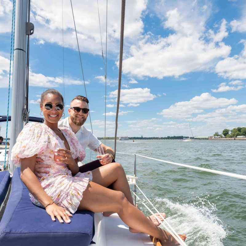 Smiling couple after a proposal on a sailboat near the Statue of Liberty on a sunny day in NYC.