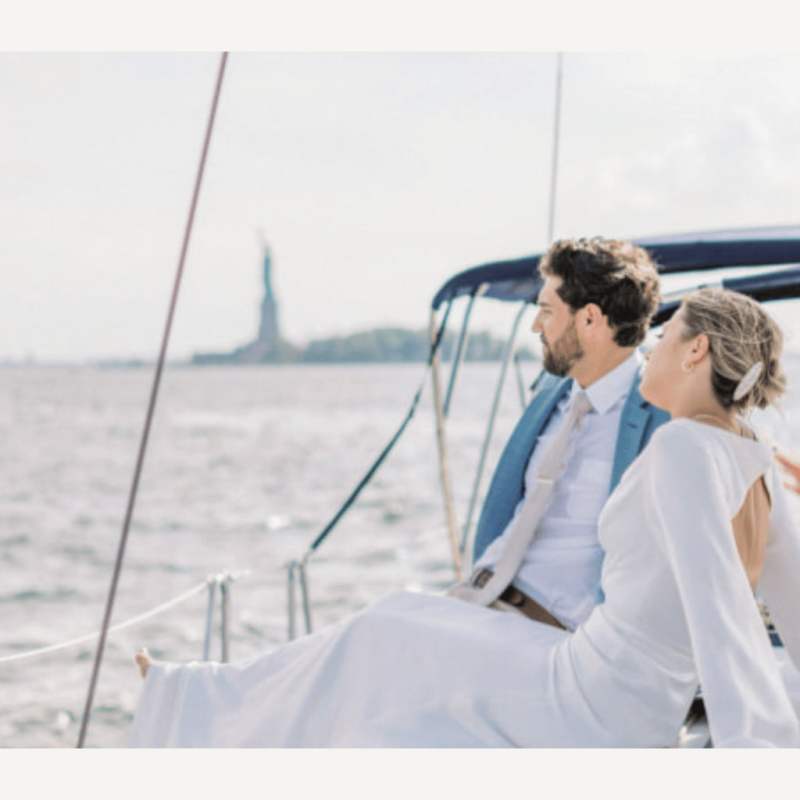 Couple in formal attire on a sailboat with Statue of Liberty in the background.