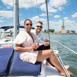 Couple on a romantic boat rental NYC sitting on a private sailboat with the Statue of Liberty in the background.