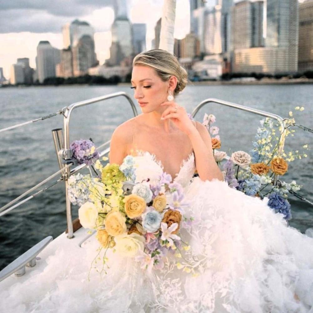 Bride in white gown with bouquet on a romantic boat ride during sunset with the NYC skyline in background.