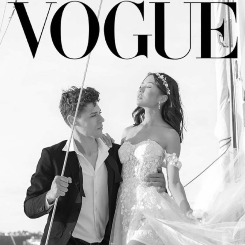 Couple in elegant attire on a boat charter under the Vogue logo.