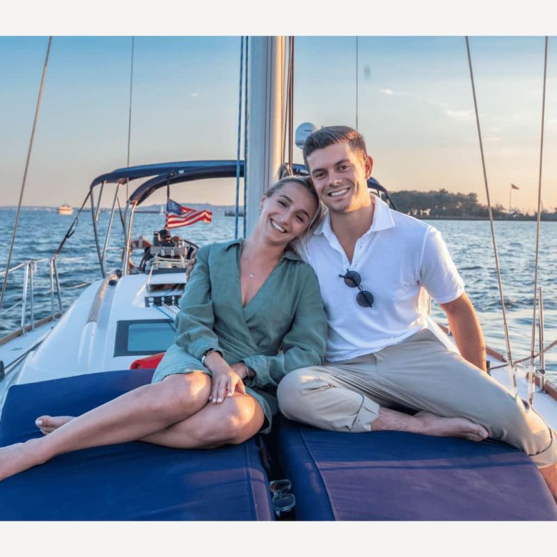 Smiling couple on a sail in NYC at sunset with water in the background.