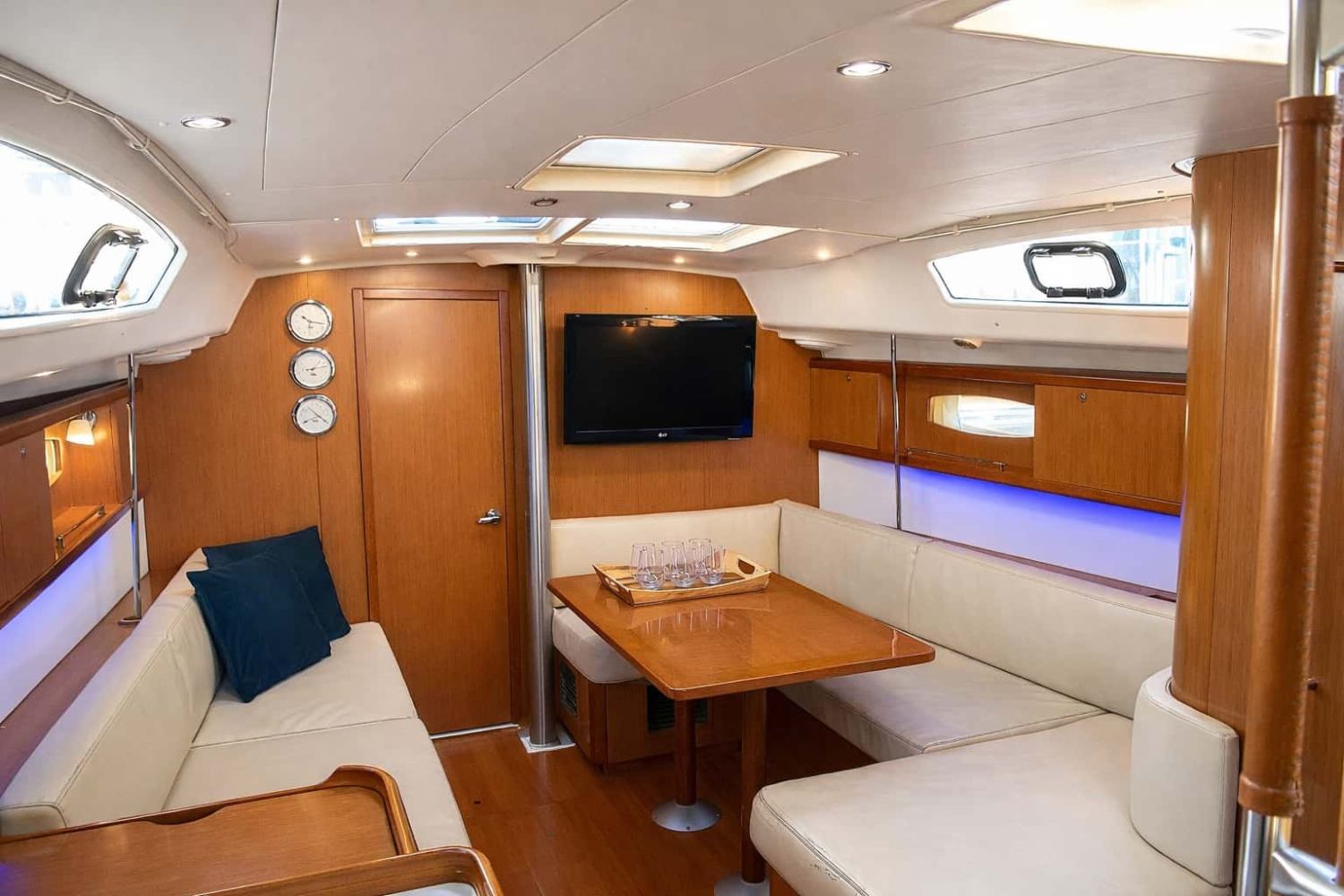 modern indoor cabin on NYC sailboat charter with C-shaped seating, chessboard on table, and wall-mounted TV, providing comfort during weather changes.