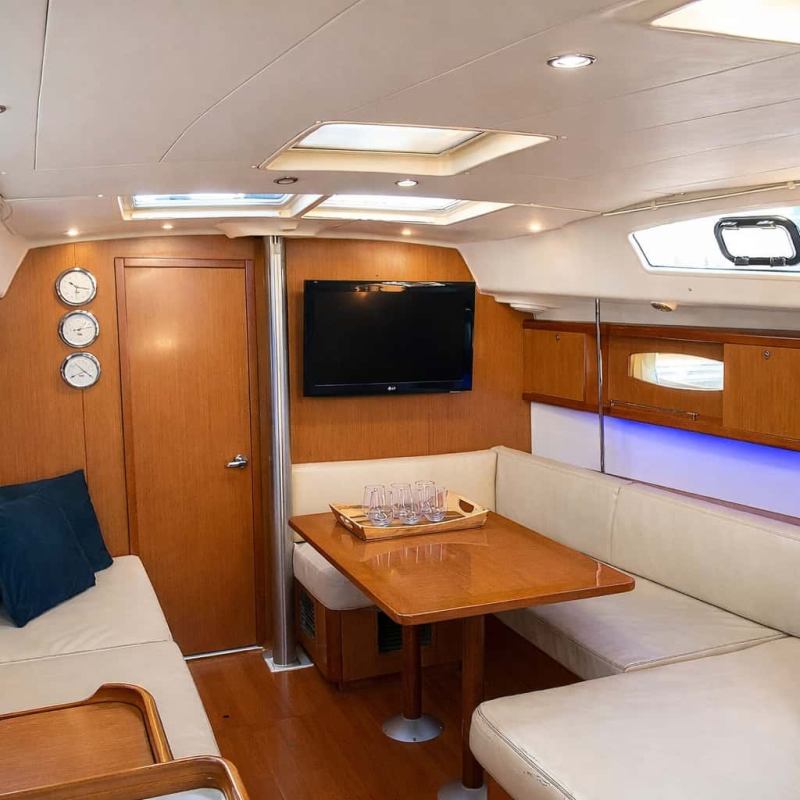 Interior of a sailboat charter in NYC with wooden panels, white couches, a TV, and a small dining table.