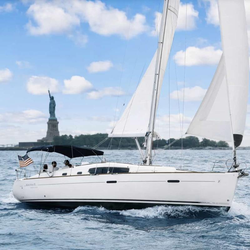 White sailboat charter in NYC with Statue of Liberty in the background under a partly cloudy sky.