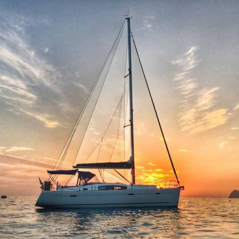 Sailboat on calm water at sunset with colorful sky and clouds.