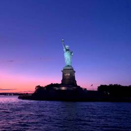 Statue of Liberty silhouetted against a colorful sunset sky over water during a sail in NYC.