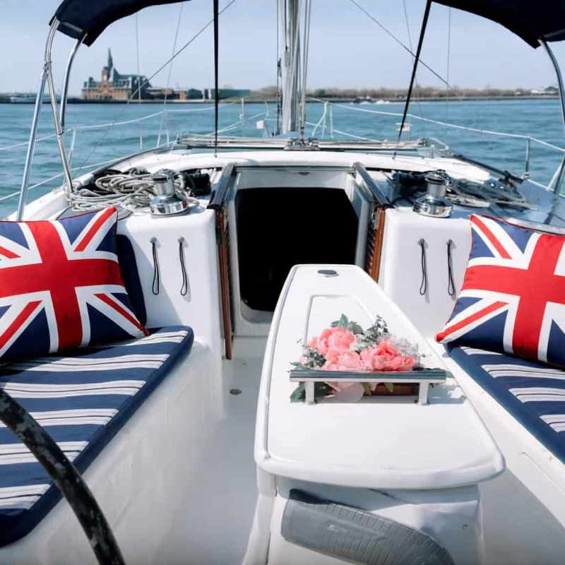 Boat deck with Union Jack cushions and pink flowers, surrounded by water.