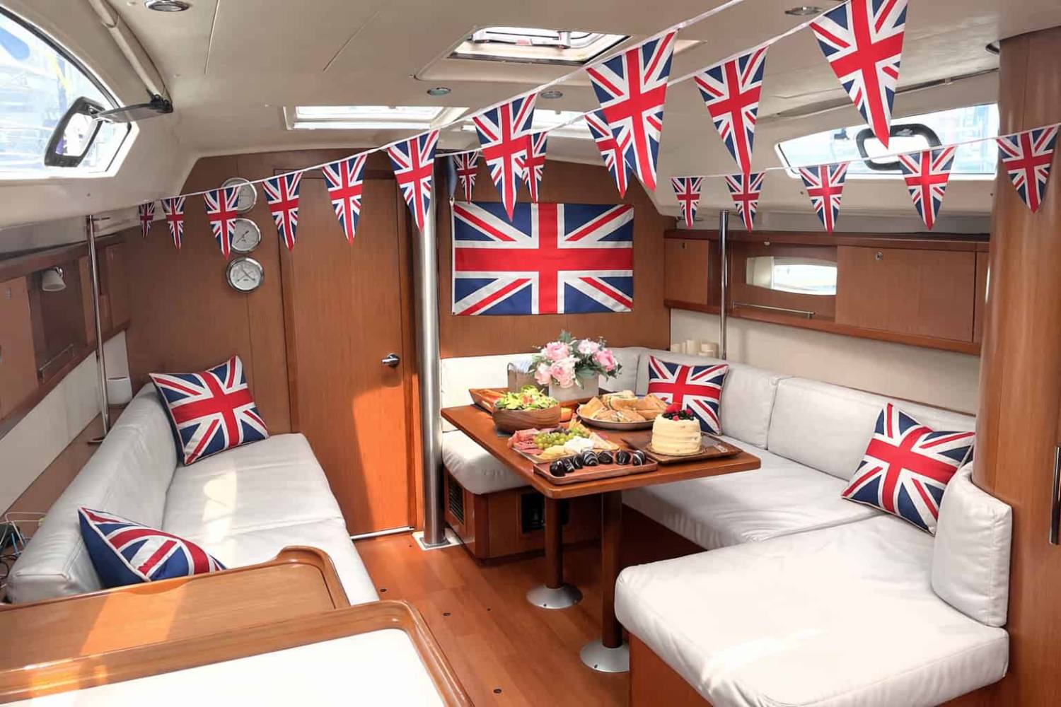 Boat interior decorated with Union Jack flags and cushions, table set with food and flowers.