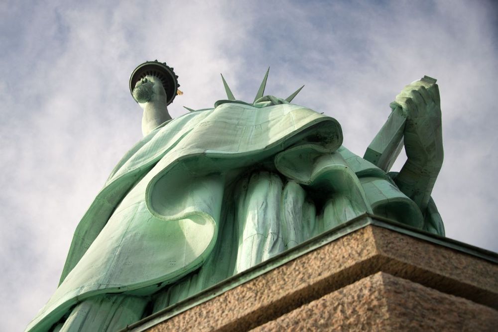 Low-angle view of the Statue of Liberty against a cloudy sky.