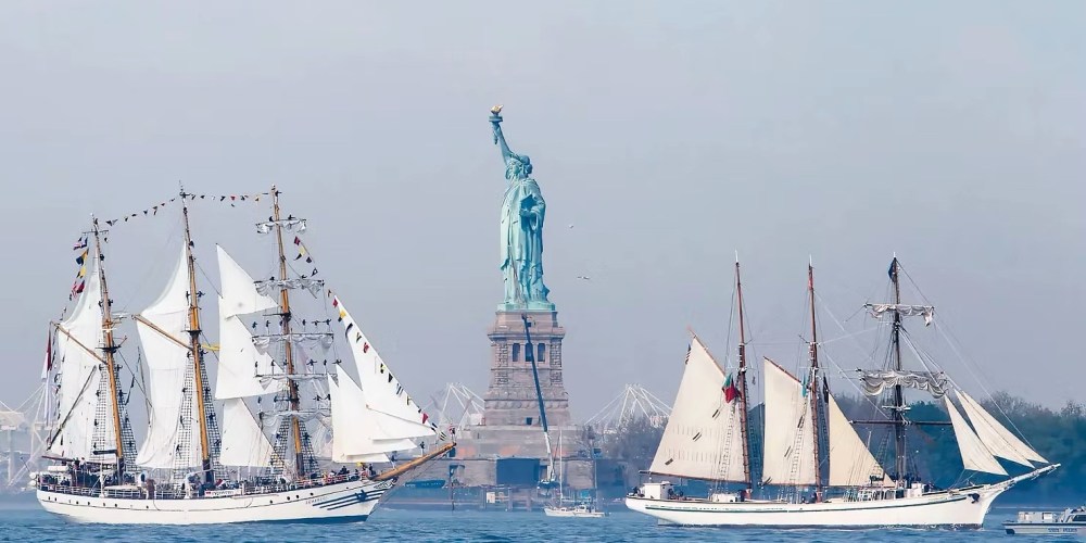 Sailboats on the water with Statue of Liberty in the background for the Sail4th 250 NYC Tall Ships Parade