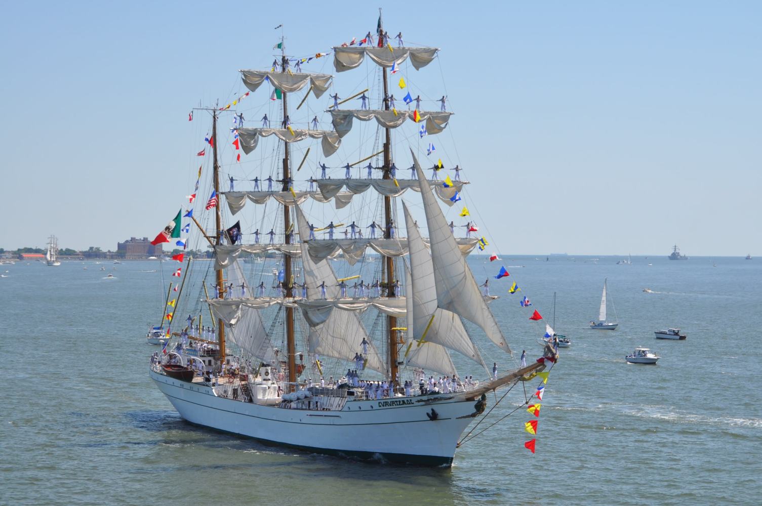 Tall ship with sails and colorful flags on a calm sea.