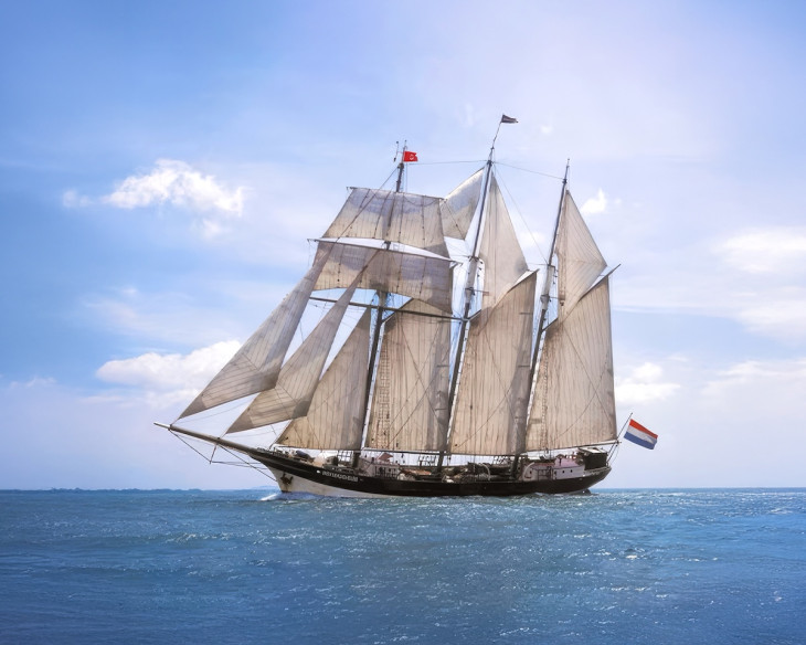 Tall ship with sails open on a sunny day at sea.